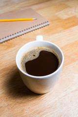 Cup of coffee and notebook on wooden table.