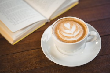 Cup of cappuccino with coffee art next to opened book