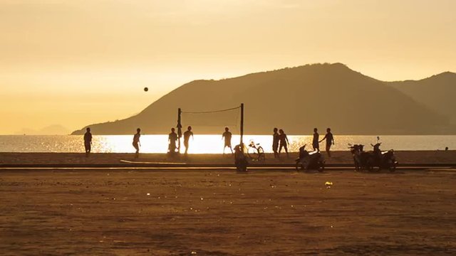 men play volleyball on beach against sunlight path at sunrise	