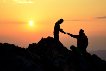 Two friends helping each other and with teamwork trying to reach the top of the mountains during wonderful summer sunrise.