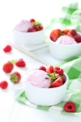 Ice cream in bowl with strawberries and raspberries on white woo