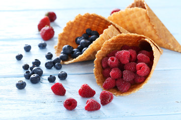 Waffle cones with berries on wooden table