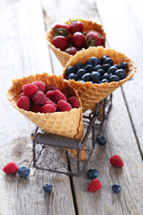 Waffle cones with berries on wooden table