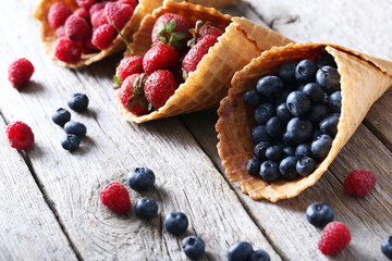 Waffle cones with berries on wooden table