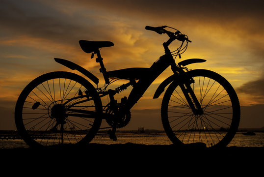 Silhouette of mountain bike with sunset sky beside sea
