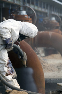 Worker in protective equipment cleans the metal construction before painting them
