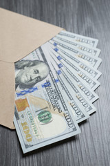 Hundred dollar banknotes in an open envelope on black wooden table