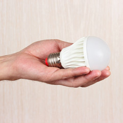 Hand holding ecofriendly led bulb on a light wood background