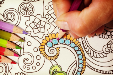 An image of a new trendy thing called adults coloring book.  In this image a person is coloring an illustrative and detailed pattern for stress relieve . Image has a vintage effect applied.