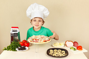 Young funny boy in chefs hat shows how to cook a pizza
