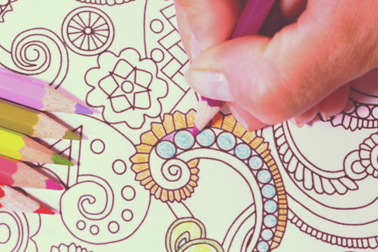 An image of a new trendy thing called adults coloring book.  In this image a person is coloring an illustrative and detailed pattern for stress relieve . Image has a vintage effect applied. 