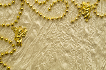 Wedding or celebration background with golden beads and angel figures on the white silk textile.