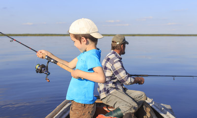Obraz premium Fishing with spinning. Grandfather and grandson fishing together on a spinning sitting in a boat on a river
