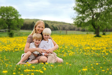 Happy Young Mother and Two Children Sitting in Flower Meadow