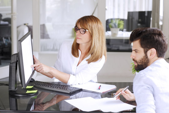 Portrait of group of business people consulting at office. Mature businesswoman sitting in front of white screen computer and presenting business plan while analyzing financial data.