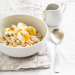 oatmeal with banana, caramel sauce  in a white bowl on a light surface, a delicious and healthy Breakfast