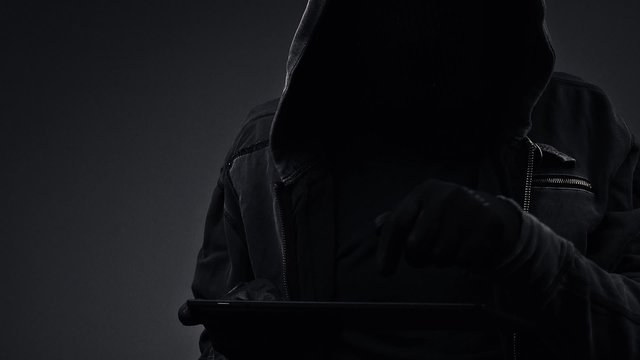 Unrecognizable faceless hooded cyber criminal using digital tablet computer to access internet web page, p2p and piracy concept, hd footage