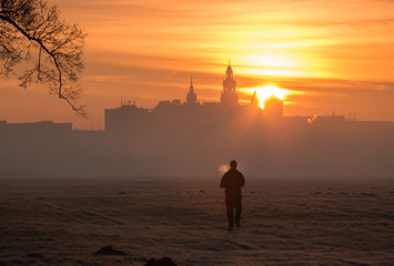 Lonely runner in the morning hoarfrost on Blonia meadow, with silhouette of Wawel castle in Krakow and rising sun as a background