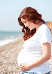 Happy pregnant girl holding big tummy outdoors. Posing over sea background. Motherhood. Maternity. 