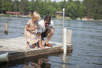 Young girl feeds fish from a dock in Minnesota with her father