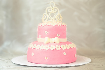 Pink cake with a crown on a white plate over a white tablecloth
