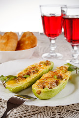Zucchini stuffed with meat, cheese and garlic served with patties and glasses of red wine on white lacy napkin