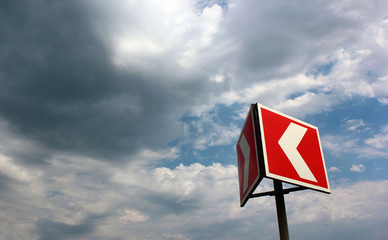 Red and white warning arrow on cloudy sky background