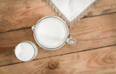 Jug, glass of milk and delicate cloth on an old wooden table. top view