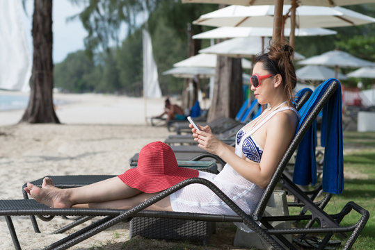 Asian woman using smart phone on beach chair