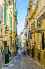 People are passing by through narrow streets of historical old town in italian naples.
