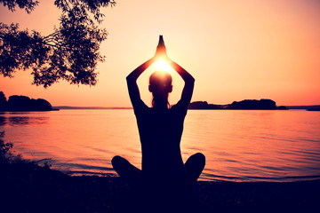 Silhouette woman practicing yoga posing on beach at sunset