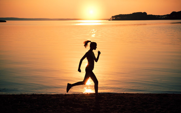 Silhouette woman jogging on beach at sunset