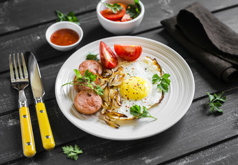 fried egg, sausage, tomatoes - tasty Breakfast or snack, on the bright plate on a dark wooden background