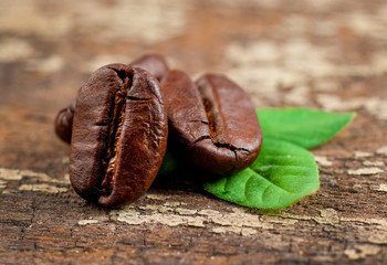 Obraz premium Coffee grains and green leaf on grunge wooden background