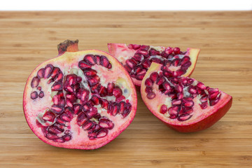 Close-up of a ripe pomegranate (Punica granatum) cut in half and split on a wooden chopping board.