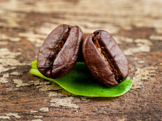 Coffee grains and green leaf on grunge wooden background