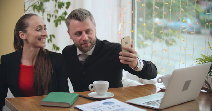 Businessman and businesswoman taking some selfies during meeting at café 
