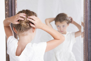 Child fixing her hair while looking in the mirror.