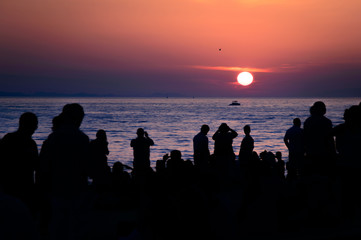 Silhouettes of people watching and filming sunset over the sea o