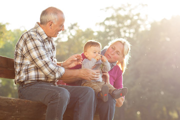 Grandparents with grandson enjoying the sunny autumn day in park.