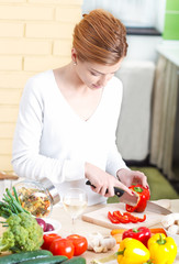 Smiling young woman cutting vegetables in kitchen.