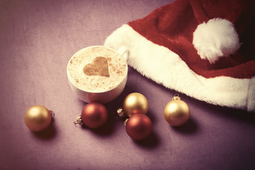Cup of coffee with heart shape near Santas hat