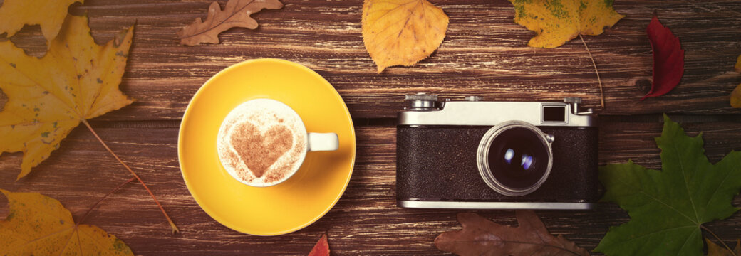 Autumn leafs, camera and coffee cup on wooden table.