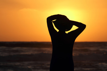 Fototapeta premium female form with the hat against the sea at sunset