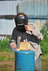 Welder in black mask woks outdoor with metal tube