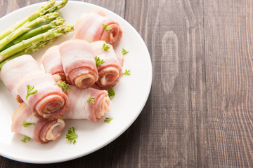Bacon rolls with asparagus on wooden background
