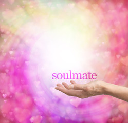 Seeking a soulmate - female hand palm up with the word Soulmate floating above, surrounded by a spiral of pastel colored soft focus love hearts on a bokeh background