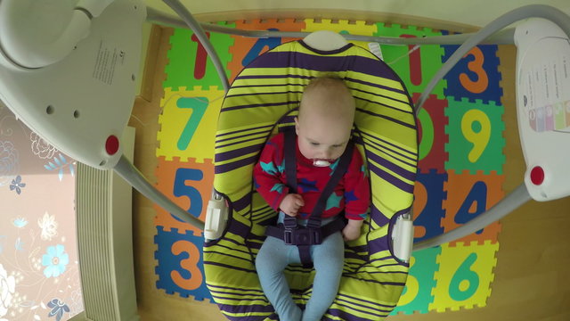 5 month baby girl swing in electric bounce swing at home. 4K UHD wide angle shot. Camera hang on swing handle.
