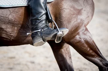 Tuinposter Paardrijden Closeup of a foot in a stirrup with a brown horse.