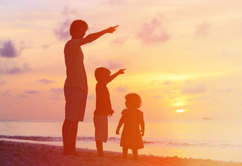 Fototapeta premium father and kids at sunset beach, pointing to the sun